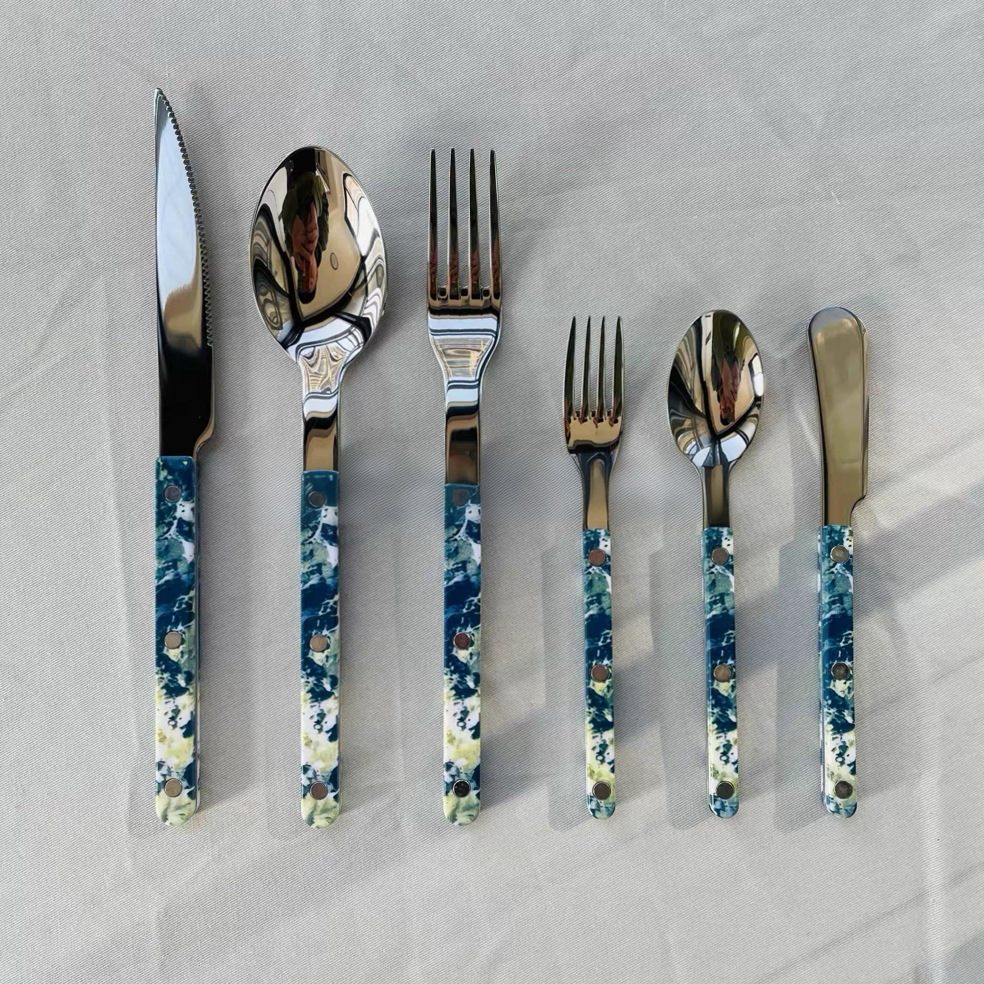 Set of silver cutlery with blue and white patterned handles on a light gray background