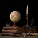 Vintage globe on books with a candle and quill pen against a dark background