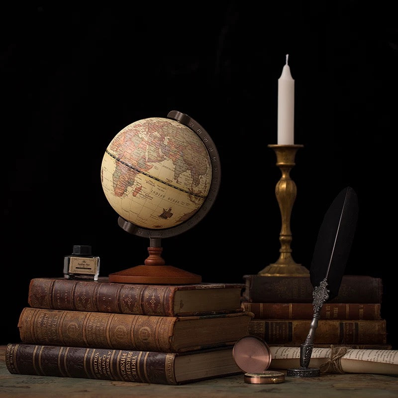 Vintage globe on books with a candle and quill pen against a dark background